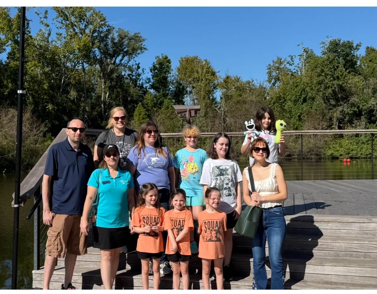 Un grupo de personas, entre adultos y niños, sonríen en una terraza de madera junto a un lago.