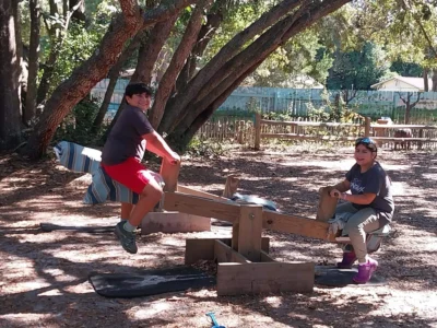 Dos niños jugando en un balancín en un parque soleado.