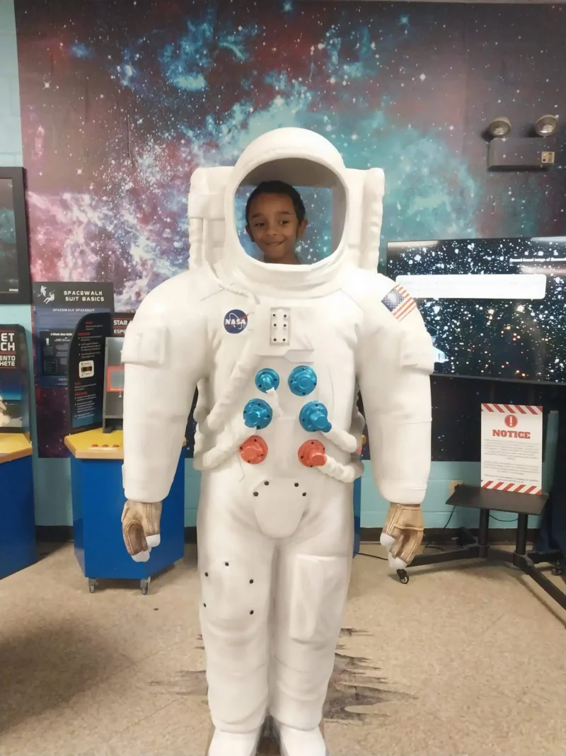 Niño sonriendo desde un recorte de traje de astronauta en una exposición espacial.